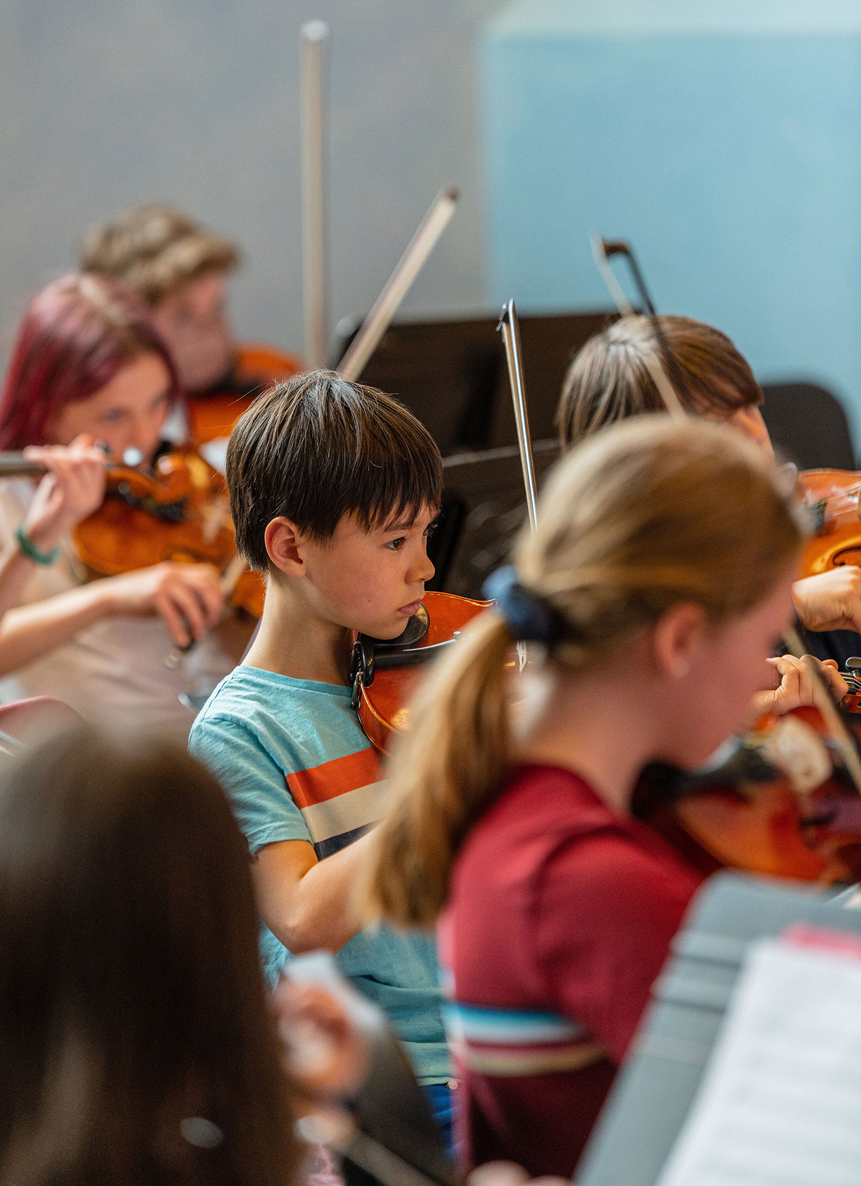 Middle school students in strings class; focus is on a young boy wearing a blue shirt and playing the violin