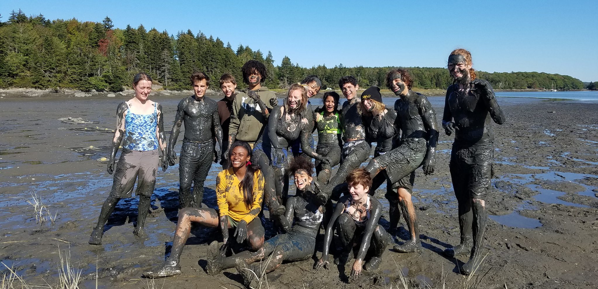 Senior class on Hermit Island trip poses while covered in mud at the beach