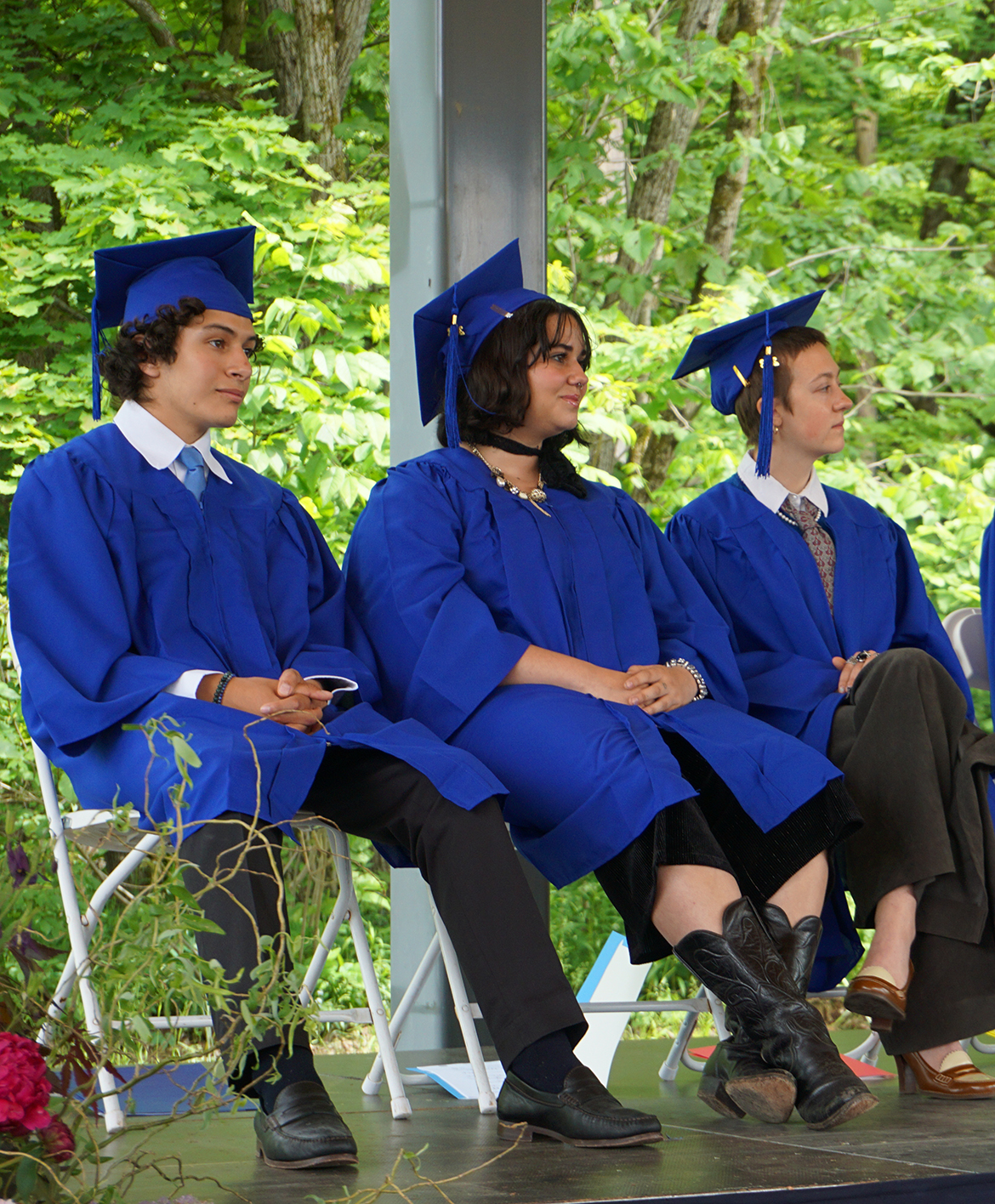 Three students - one male and two female - wearing blue graduation caps and gowns seated on a stage beneath our open air pavilion