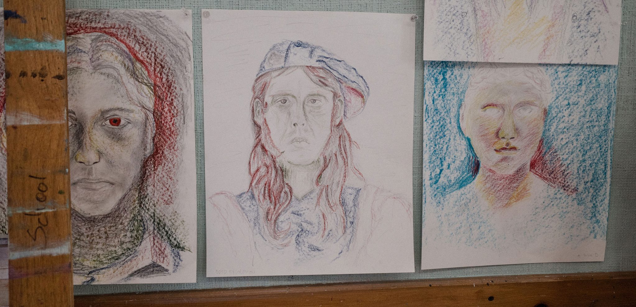 three self-portrait sketches made by seniors hang on a bulletin board