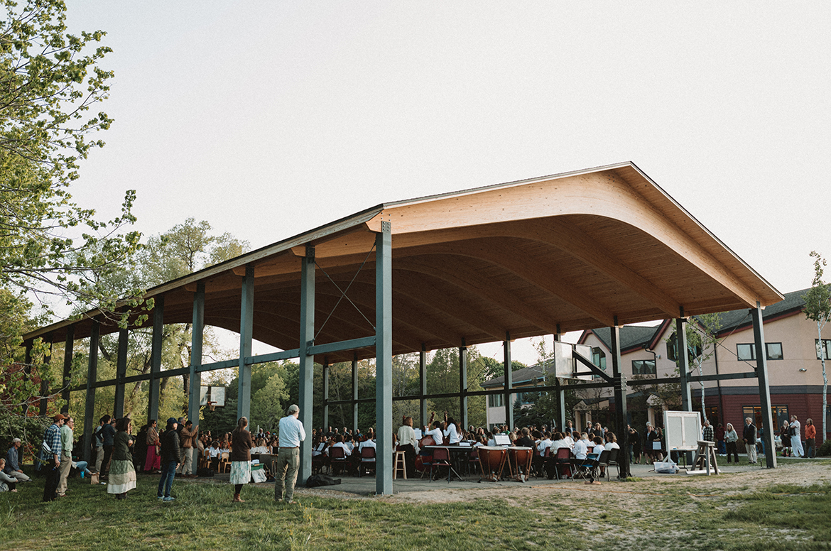 View of new school open air pavilion during a 2023 spring concert; there are students seated performing beneath the pavilion