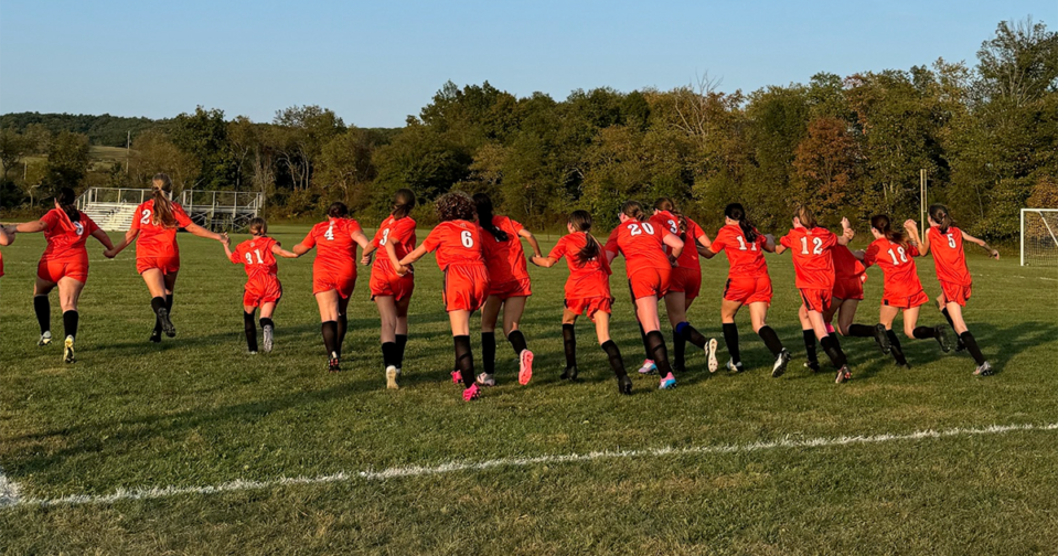 Girls modified soccer team running on the field together holding hands